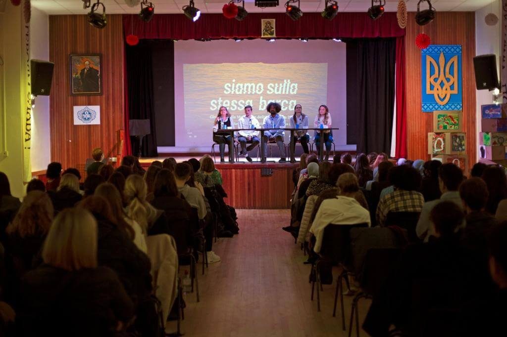 Un auditorium pieno di pubblico che ascolta cinque persone su un palco